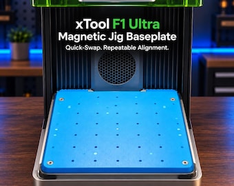May include: A blue magnetic jig baseplate for the xTool F1 Ultra laser machine. The rectangular plate features a grid of small holes for alignment and is installed within the black metal housing of the device, which has a green top cover.