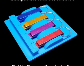 May include: A blue 3D printed jig for making bottle opener keychains. The jig holds four bottle openers in different colors: blue, gold, purple, and red. The jig is compatible with the xTool F1.