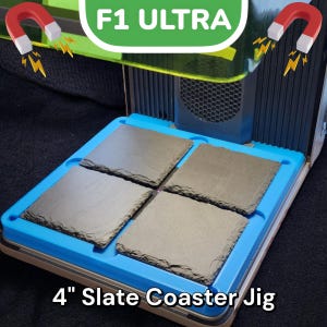 May include: A blue and white jig for making 4-inch slate coasters. The jig is made of plastic and has four slots for the coasters. The jig is sitting on a black surface. The text "F1 ULTRA" is visible in the background.