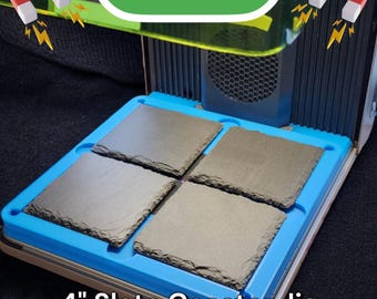 May include: A blue and white jig for making 4-inch slate coasters. The jig is made of plastic and has four slots for the coasters. The jig is sitting on a black surface. The text "F1 ULTRA" is visible in the background.