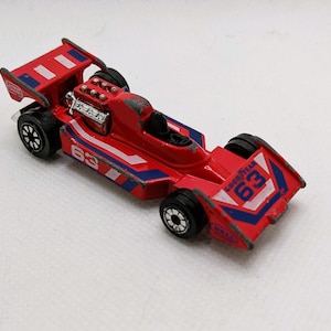 May include: Red and blue toy race car with the number 63 on the side. The car has a detailed engine and a spoiler.