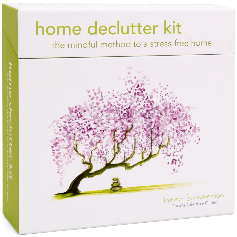 K&ouml;nnte beinhalten: Eine wei&szlig;e Box mit gr&uuml;nem Rand, auf der der Text "home declutter kit" und "the mindful method to a stress-free home" steht. Die Box zeigt eine Aquarell-Illustration eines rosa bl&uuml;henden Baumes mit einem gr&uuml;nen Stamm und einem Stapel grauer Steine an der Basis. Der Text "Helen Sanderson Creating Calm from Clutter" befindet sich am unteren Rand der Box.