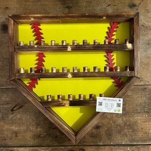 May include: A wooden softball display case with two shelves and a yellow background. The case is shaped like a baseball diamond and has red stitching around the edges. The case is made by DBR Woodwork.