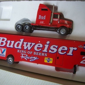 May include: A red toy semi-truck and trailer with the Budweiser logo and the text "King of Beers Racing". The trailer also has the Valvoline and Pedigree logos. The truck has the text "Bud" on the side.