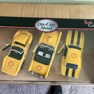 May include: A set of three yellow die-cast metal cars in a box. The cars are a Chevrolet Corvette, a Ford Mustang, and a Chevrolet Camaro. Each car has a Shell logo on the side. The box says "Die-Cast Metal" and "Scale 1:34-38 Collection".