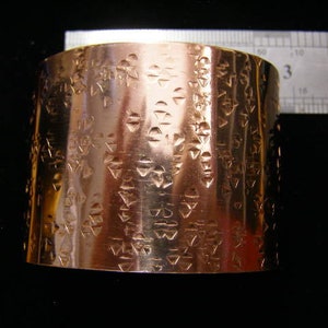 May include: A copper bracelet with a geometric pattern embossed on the surface.