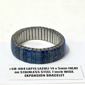 May include: A stainless steel expansion bracelet with a 7-inch width, featuring a lapis lazuli inlay. The bracelet has a rectangular design with a dark blue color. The text on the label reads "#EB-004 LAPIS LAZULI 14 x 5mm INLAY on STAINLESS STEEL 7 inch WIDE EXPANSION BRACELET."