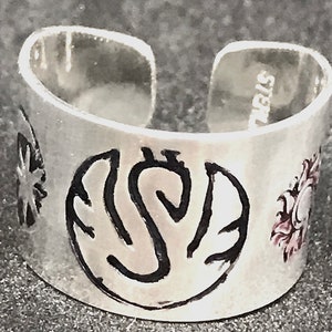 May include: Silver adjustable ring with a black and white design of a stylized sun, moon, and star. The ring is engraved with the word "Sterling".