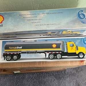 May include: A model Formula Shell tanker truck in a box. The truck is yellow and gray with the Shell logo. The box has text that says "Working Headlights, Taillights, and Running Lights". The box also says "6th in a series."