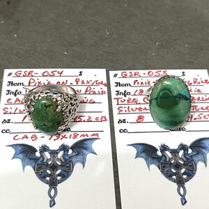 May include: Two sterling silver rings with turquoise cabochon stones. One ring has an openwork design around the stone, while the other has a simple band. The rings are displayed on cards with handwritten details.