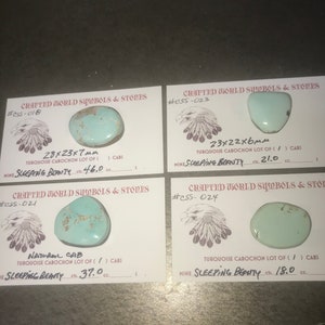 May include: Four turquoise cabochon stones on white cards with black text. The cards are labeled with the text "CRAFTED WORLD SYMBOLS & STONES" and a number. The stones are labeled with their size and carat weight. The stones are from the "SLEEPING BEAUTY" mine.