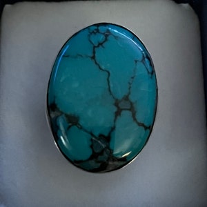 May include: A turquoise ring with a silver setting. The turquoise stone has a marbled pattern with black veins.