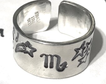 May include: Silver adjustable ring with a star, a shooting star, and the astrological symbol for Scorpio engraved on it. The ring is marked "925 Sterling".