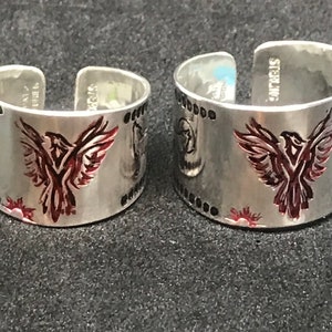May include: Two silver rings with a red phoenix design. The rings are engraved with "STERLING" on the side.