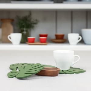 May include: Two green leaf-shaped coasters with a wooden coaster in the center. The coasters are made of a material that looks like silicone.