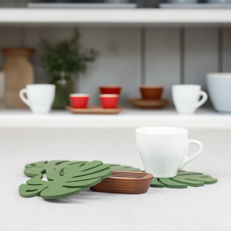 May include: Two green leaf-shaped coasters with a wooden coaster in the center. The coasters are made of a material that looks like silicone.