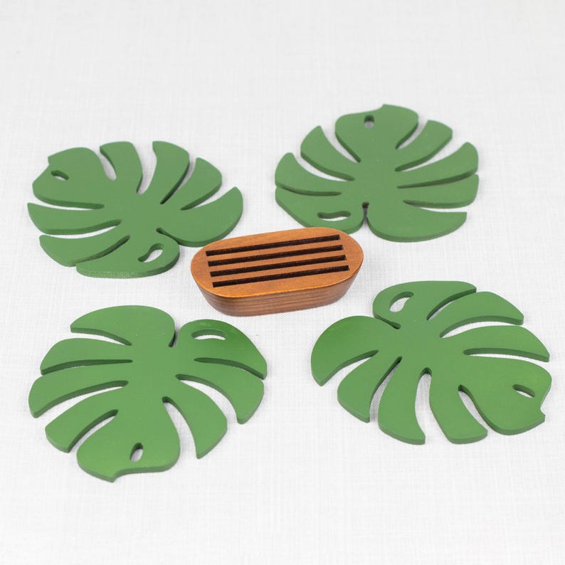 May include: Four green monstera leaf-shaped coasters with a wooden coaster in the center.