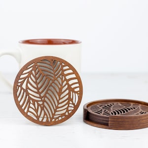 May include: Set of six brown wooden coasters with a leaf design. The coasters are stacked on top of each other.