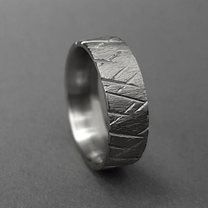 Puede incluir: Un anillo de plata con un patrón geométrico texturizado. El anillo está hecho de metal y tiene un acabado pulido.