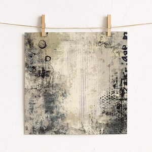 May include: Abstract art print with a neutral colour palette. The artwork features a mix of textures, including brushstrokes, splatters, and vertical lines. The colour scheme includes shades of beige, grey, and black, creating a modern and minimalist aesthetic. The print is held by wooden pegs.
