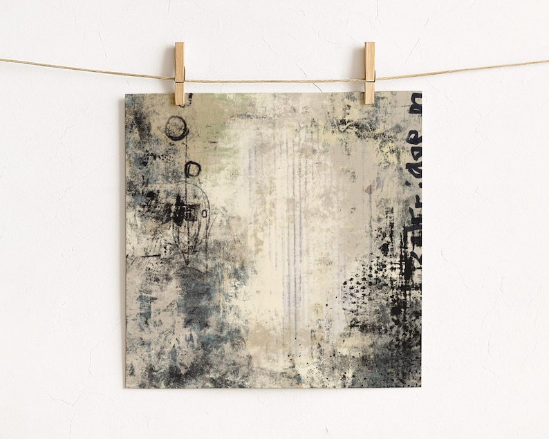 May include: Abstract art print with a neutral colour palette. The artwork features a mix of textures, including brushstrokes, splatters, and vertical lines. The colour scheme includes shades of beige, grey, and black, creating a modern and minimalist aesthetic. The print is held by wooden pegs.