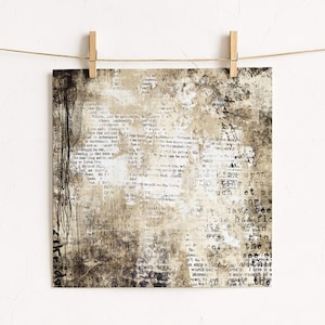 May include: Square art print with a vintage aesthetic, featuring a collage of text and abstract textures in shades of beige, brown, and white. The print is held by wooden pegs on a string, creating a rustic display.