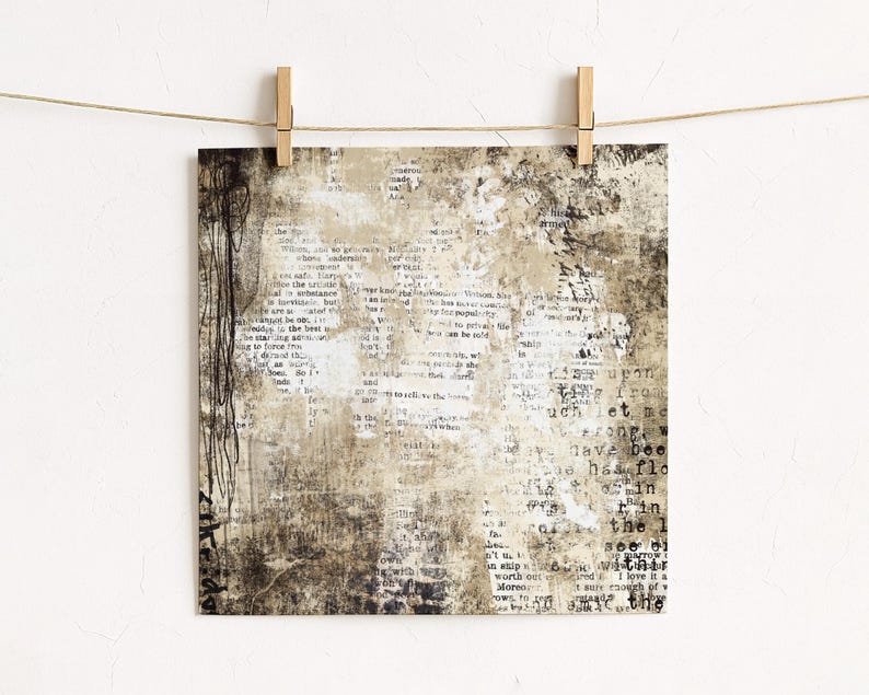 May include: Square art print with a vintage aesthetic, featuring a collage of text and abstract textures in shades of beige, brown, and white. The print is held by wooden pegs on a string, creating a rustic display.