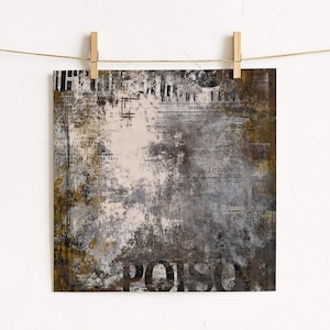 May include: Square abstract art print with a distressed, textured design. The artwork features a mix of neutral colours, including brown, grey, and white, with visible text elements and the word "POISON" in large, bold letters. The print is held by wooden clips.