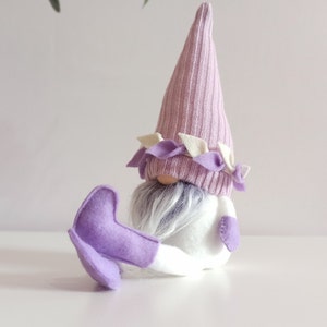May include: A purple and white gnome with a long, pointed hat and a white beard. The gnome is wearing purple boots and has a white body.