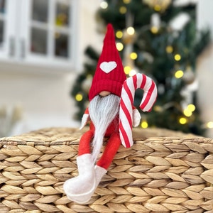 May include: A red and white gnome figurine with a white heart on its hat, holding a candy cane. The gnome is sitting on a woven wicker basket.