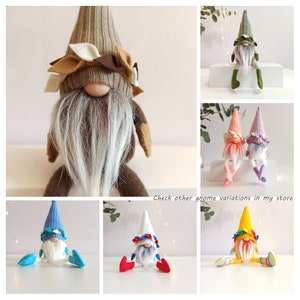 May include: A collection of ten handmade gnomes with different colored hats and outfits. The gnomes are sitting on a white surface. The gnomes are all wearing a white beard and have a red nose. The gnomes are all wearing different colored hats and outfits. The gnomes are all handmade and unique.