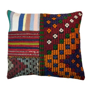 Può includere: Un cuscino patchwork colorato con un motivo geometrico. Il cuscino è realizzato in tessuto tessuto e presenta una varietà di colori, tra cui rosso, blu, verde, arancione e giallo.