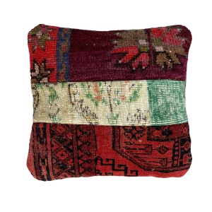 May include: A square throw pillow with a patchwork design. The pillow is made from different pieces of fabric with floral patterns in shades of red, green, and cream. The pillow has a black border.