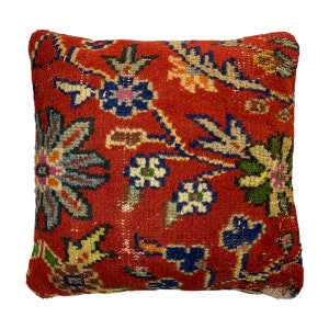 May include: Red cushion with a floral pattern in shades of blue, green, yellow, and white. The cushion is made of a soft, woven fabric.