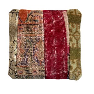 May include: A square pillow with a patchwork design. The pillow is made of four different fabrics, each with a different pattern. The fabrics are a light beige with a floral pattern, a dark red with a geometric pattern, a light green with a geometric pattern, and a light beige with a floral pattern. The pillow is perfect for adding a touch of bohemian style to any room.