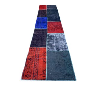 May include: A long, rectangular patchwork rug with a variety of colors and patterns. The rug is made up of several different pieces of fabric, including red, blue, black, and white. The rug has a fringed edge.