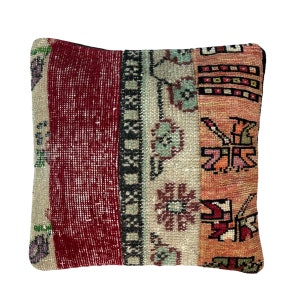 Pode incluir: Uma almofada quadrada com um design de patchwork em tons de vermelho, bege e laranja. A almofada tem um padrão tradicional turco kilim com motivos florais e geométricos.