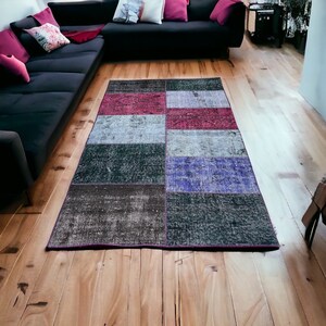 Può includere: Un tappeto patchwork multicolore con diverse tonalità di blu, viola, rosa e grigio. Il tappeto è realizzato con diversi tessuti e trame, creando un aspetto unico ed eclettico.