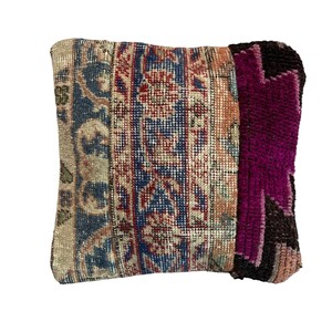 May include: A decorative pillow with a patchwork design featuring a mix of floral patterns in shades of red, blue, and beige. The pillow is made from a woven fabric with a textured surface. The back of the pillow is a solid dark purple.