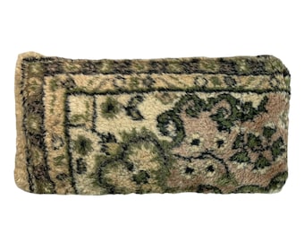 May include: A rectangular pillow with a plush, fuzzy texture. The pillow features a brown, green, and cream patterned design reminiscent of a traditional rug.