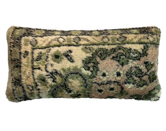 May include: A long, rectangular pillow with a green, brown, and beige patterned fabric. The fabric has a fuzzy texture and resembles a rug.