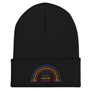 May include: Black knit beanie with a rainbow design embroidered on the front. The rainbow is made of five different colored lines, with a wavy line underneath.