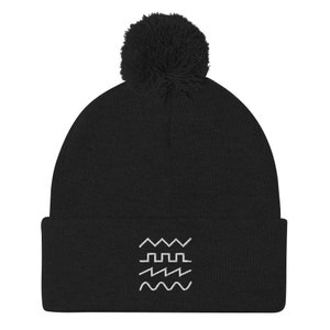Puede incluir: Gorro negro con un diseño bordado blanco de diferentes formas de onda. El gorro tiene un pompón negro en la parte superior.