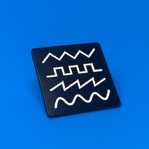 May include: A square, black pin with three white wave-like designs. The pin is set against a bright blue background. The designs include a sawtooth wave, a square wave, and a sine wave.