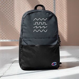 Puede incluir: Una mochila negra y gris con un diseño bordado blanco de diferentes formas de onda. La mochila tiene un bolsillo con cremallera negro en la parte delantera y un pequeño logotipo de Champion rojo y azul en la esquina inferior derecha.