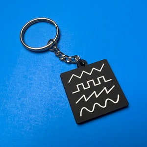 May include: A black keychain with a silver key ring and a black tag with white wave patterns. The tag has four different wave patterns.