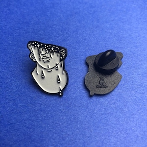 Puede incluir: Un pin de esmalte blanco y negro que presenta un busto de una persona con un diseño de cielo estrellado en la cabeza y gotas negras que caen de sus ojos y cuello. La parte posterior del pin es negra con el texto "WizardPin" en blanco.