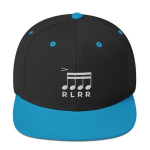 Op de afbeelding: Een zwarte en blauwe baseballpet met een wit muzieknootontwerp en de tekst "RLRR" geborduurd op de voorkant.