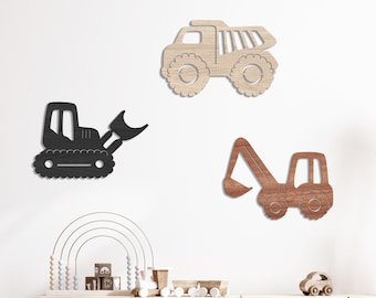 May include: A set of three wooden toy trucks in black, brown, and natural wood finishes. The trucks are in the shape of a dump truck, a bulldozer, and an excavator. The trucks are displayed on a white wall with a wooden cabinet and a chair in the background. The text "BEAR & ROSE YORK" is displayed in the top right corner of the image.
