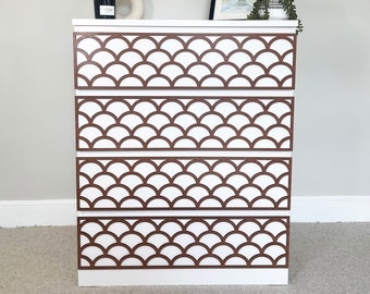 May include: White dresser with four drawers featuring a brown geometric pattern. The dresser has a modern design and is made of wood.
